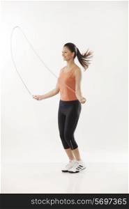 Full length of a young woman exercising with a jump rope over white background