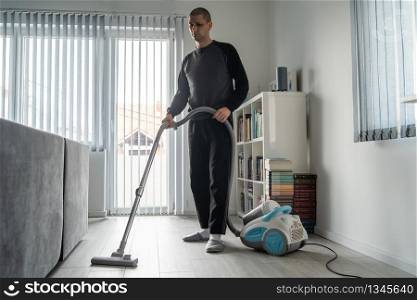 Full length of adult caucasian man using vacuum cleaner to clean the wooden floor at home vacuuming male doing housework room hygiene in day