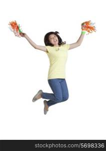 Full length of an excited young woman jumping while holding Indian tricolor pom poms over white background