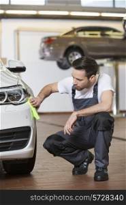 Full length of automobile mechanic cleaning car in workshop