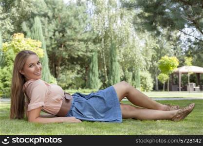 Full length of beautiful young woman reclining on grass in park