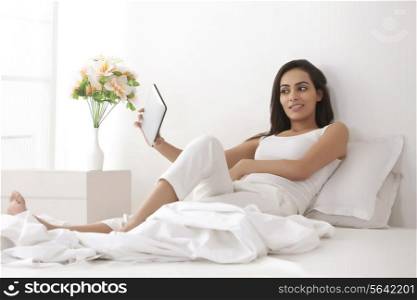 Full length of beautiful young woman taking self-portrait through digital tablet in bed