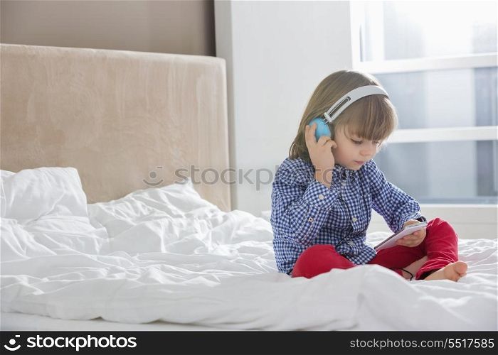 Full length of boy listening music on headphones in bedroom