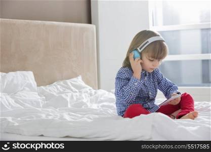 Full length of boy listening music on headphones in bedroom