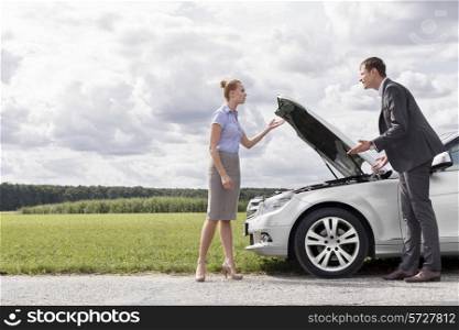 Full length of business couple arguing by broken car at countryside