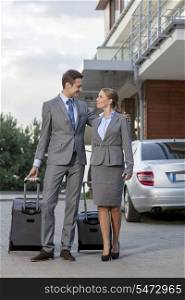 Full-length of business couple walking with luggage outside hotel