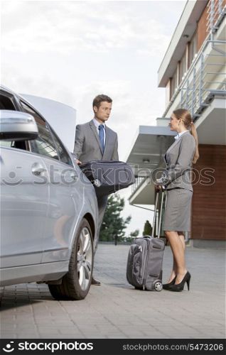 Full-length of business couple with luggage outside hotel