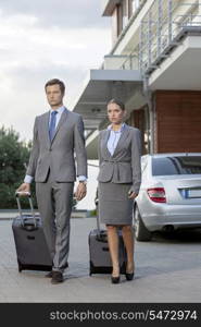 Full-length of business couple with luggage walking outside hotel