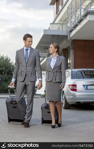 Full-length of business couple with luggage walking outside hotel
