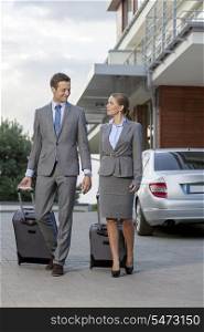 Full-length of business couple with luggage walking outside hotel