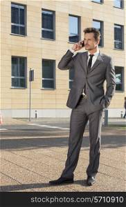 Full length of businessman conversing on cell phone against office building