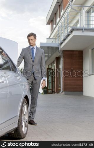 Full-length of businessman standing by car outside hotel