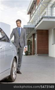Full-length of businessman standing by car outside hotel
