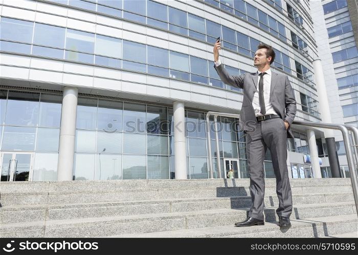 Full length of businessman taking self portrait on steps outside office
