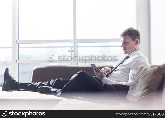 Full length of businessman using digital tablet on sofa at home