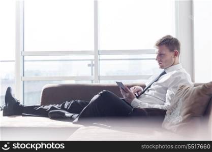 Full length of businessman using digital tablet on sofa at home