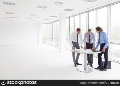 Full length of businessmen discussing over blueprints at table in new office