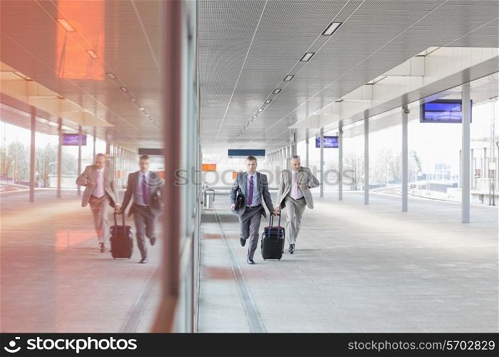 Full length of businessmen with luggage rushing on railroad platform
