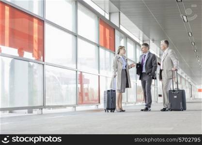 Full length of businesspeople with luggage talking on railroad platform