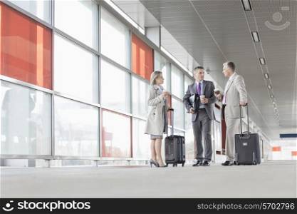 Full length of businesspeople with luggage talking on railroad platform