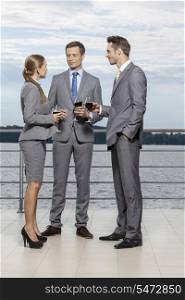 Full length of businesspeople with wineglasses standing on terrace