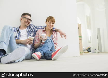 Full-length of cheerful couple with coffee cups in new house