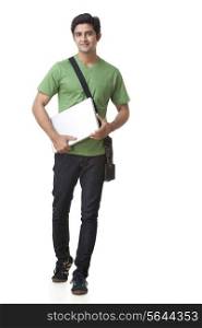 full length of college student with laptop walking over white background
