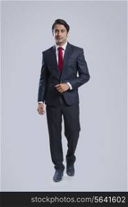 Full length of confident businessman walking against gray background