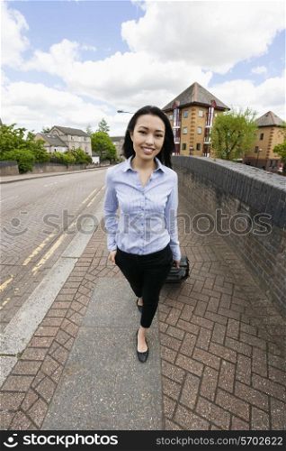 Full length of confident businesswoman with luggage walking on sidewalk