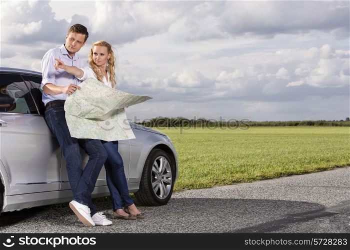 Full length of couple with map discussing direction while leaning on car at countryside
