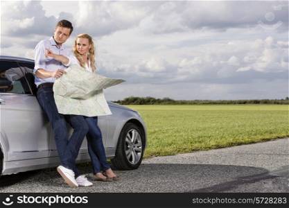 Full length of couple with map discussing direction while leaning on car at countryside
