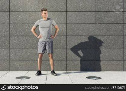 Full length of determined jogger standing against tiled wall outdoors