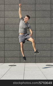 Full length of excited jogger jumping against tiled wall