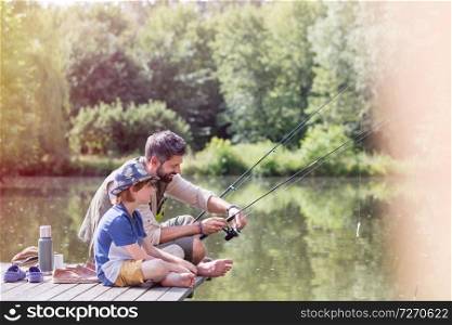Full length of father assisting son fishing in lake while sitting on pier