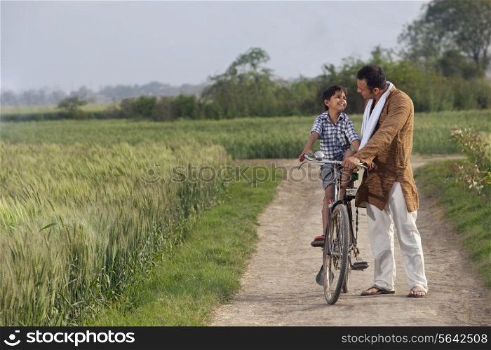 Full length of father assisting son to ride cycle