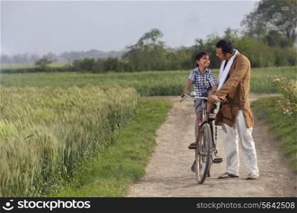 Full length of father assisting son to ride cycle