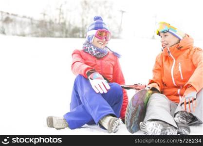 Full length of female friends with snowboard relaxing during winter