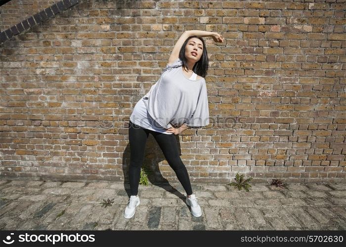 Full length of fit woman performing stretching exercise against brick wall