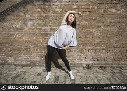 Full length of fit woman performing stretching exercise against brick wall