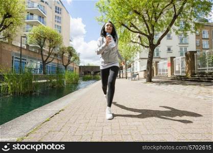 Full length of fit young woman jogging by canal against buildings