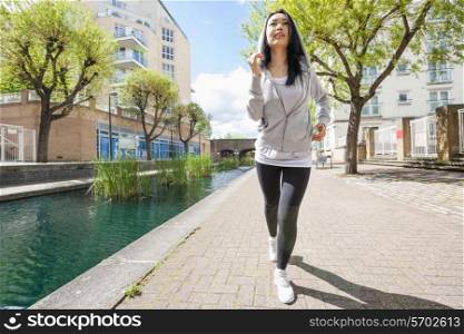 Full length of fit young woman running by canal against buildings