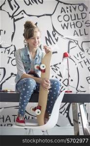 Full-length of girl with skateboard sitting on study table at home