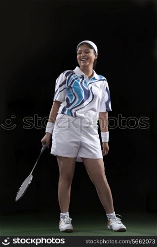 Full length of happy female player holding badminton racket isolated over black background