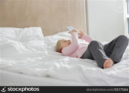 Full length of happy girl using smart phone in bed