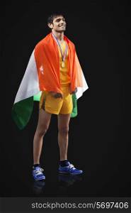 Full length of happy male medalist with Indian flag looking away against black background