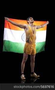 Full length of happy male medalist with Indian flag looking up over black background