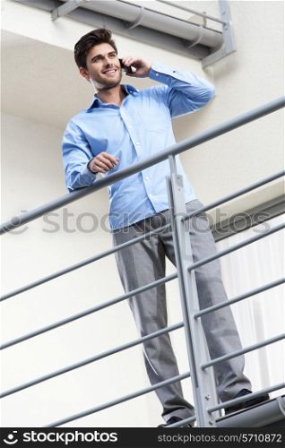 Full length of happy young businessman using mobile phone at balcony