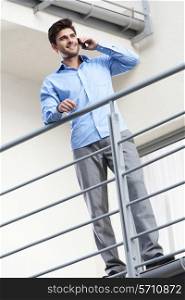 Full length of happy young businessman using mobile phone at balcony