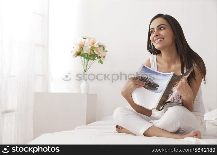 Full length of happy young woman holding magazine on bed