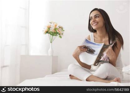 Full length of happy young woman holding magazine on bed